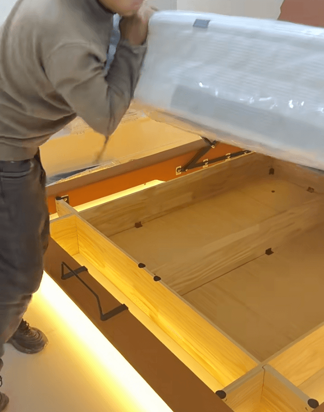 Hands compressing a failed gas lift bed strut to test nitrogen charge – a good strut is nearly impossible to compress by hand